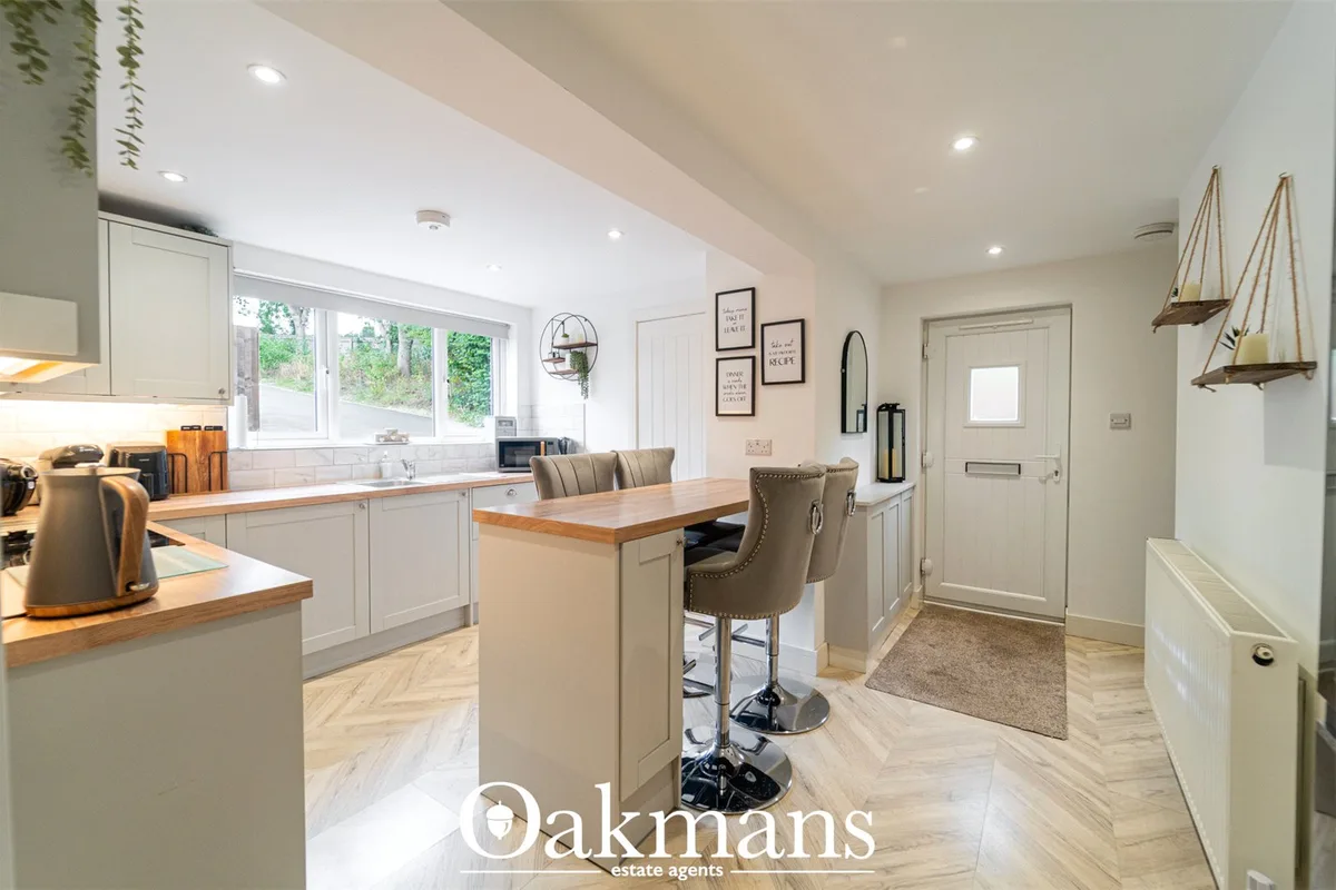 Modern kitchen with white cabinetry, wooden worktops, island with seating, and large windows overlooking garden