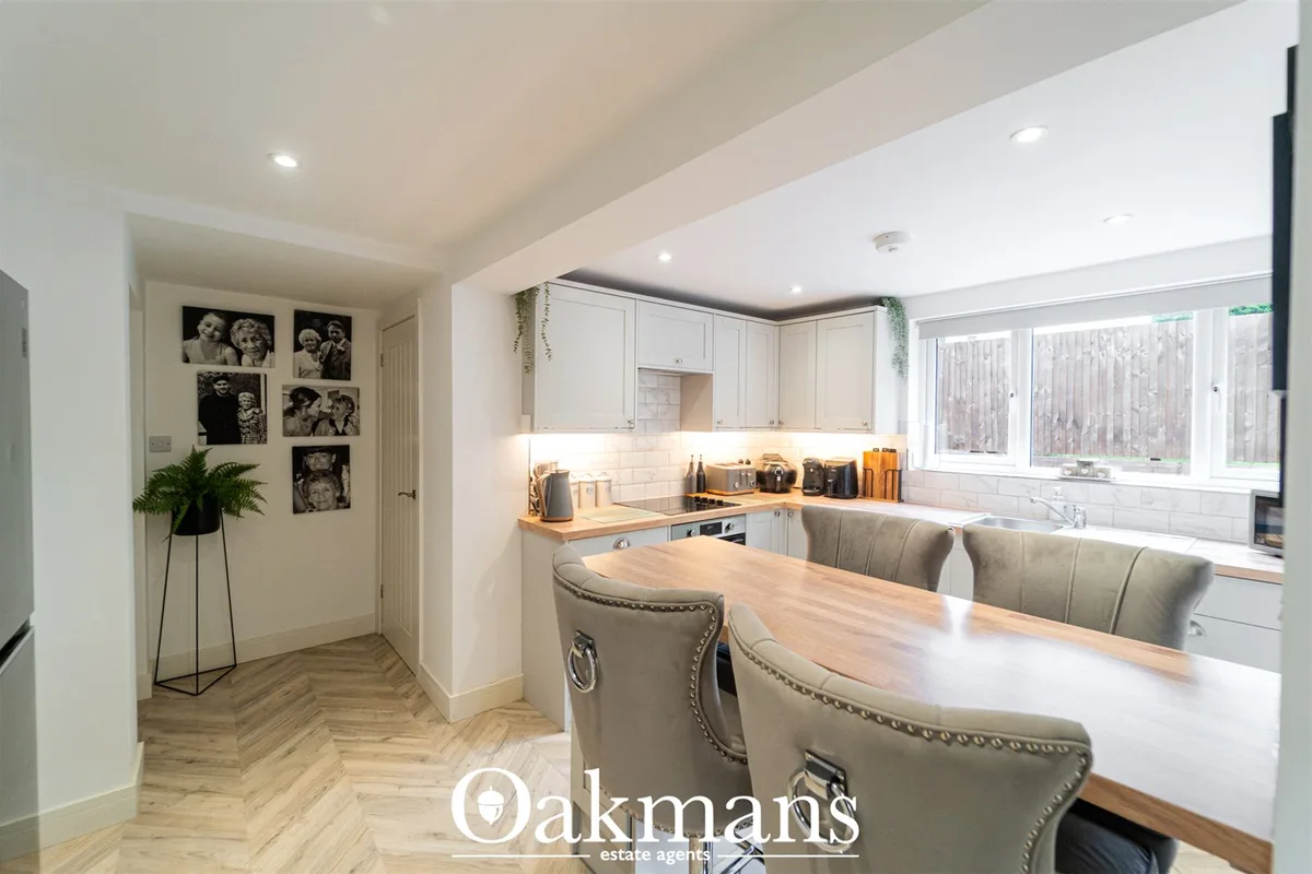 Modern white fitted kitchen with wooden worktops, subway tile splashback, breakfast bar with grey upholstered chairs, an