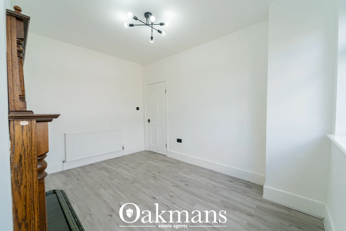 Empty bedroom with white walls, grey laminate flooring, white radiator, ceiling light fixture, white door and wooden sta