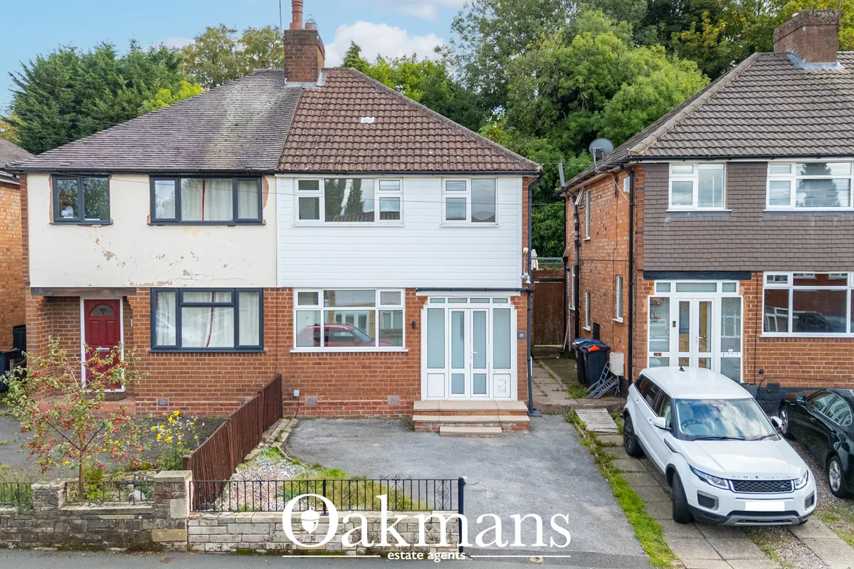 Semi-detached brick house with white rendered upper storey, tiled roof, driveway and parked cars