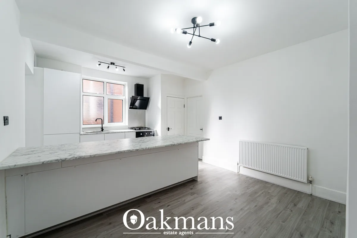 Modern white fitted kitchen with granite worktops, breakfast bar, gas hob, black extractor hood and window overlooking s