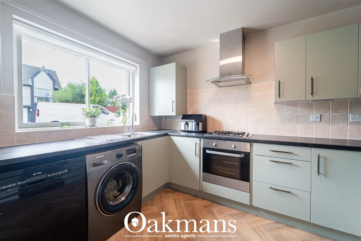 Modern fitted kitchen with cream units, black worktops, stainless steel appliances, tiled splashback, window overlooking
