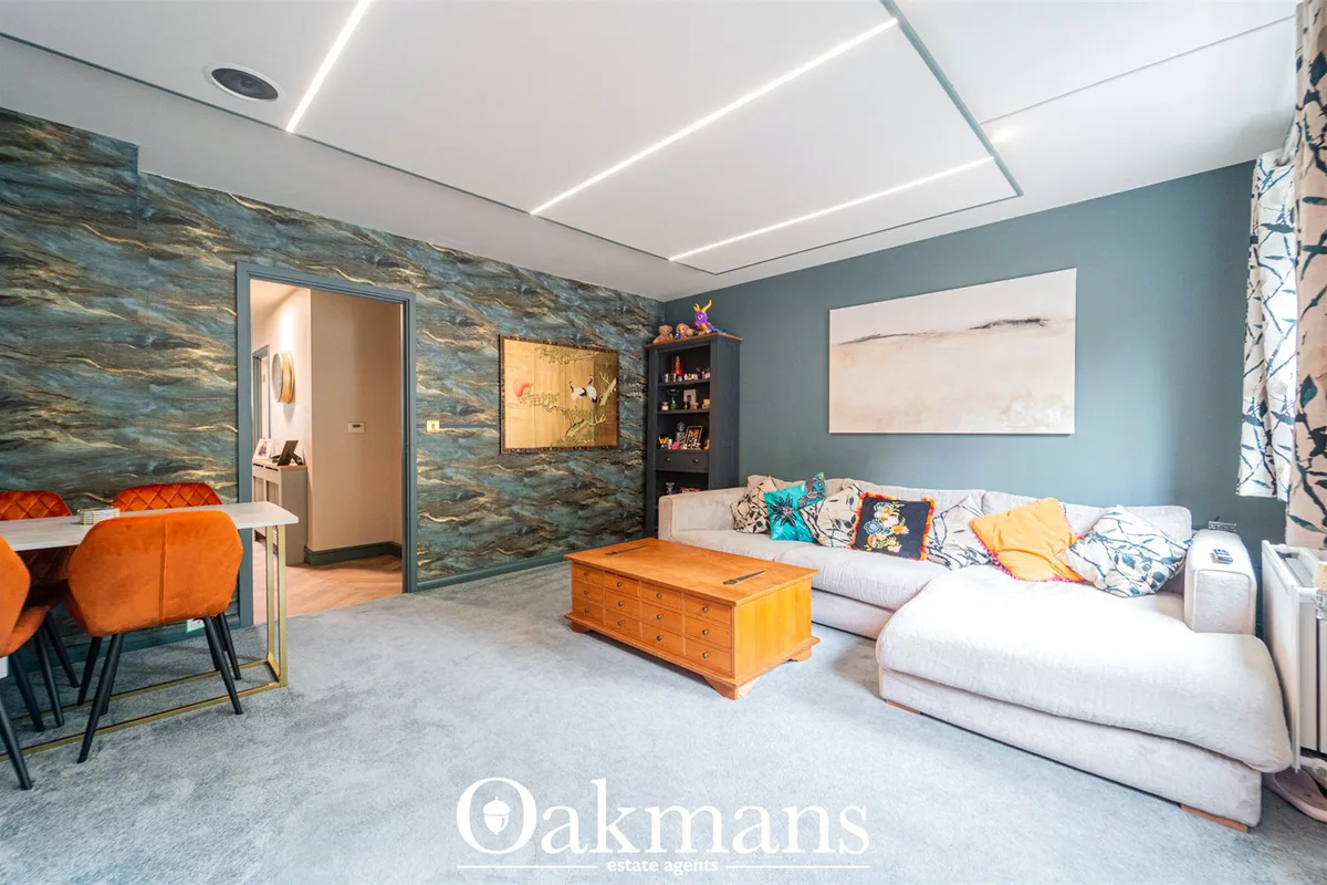 Modern living room with blue-green walls, light grey upholstered sofa with patterned cushions, wooden chest, dining area