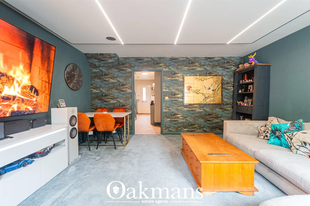 Open-plan living space with teal walls, slate feature wall, fireplace TV, orange dining chairs, cream sofa, wooden trunk
