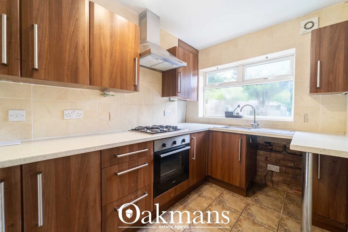 Modern fitted kitchen with walnut wood cabinets, cream tile splashback, gas hob, integrated oven, and large window overl