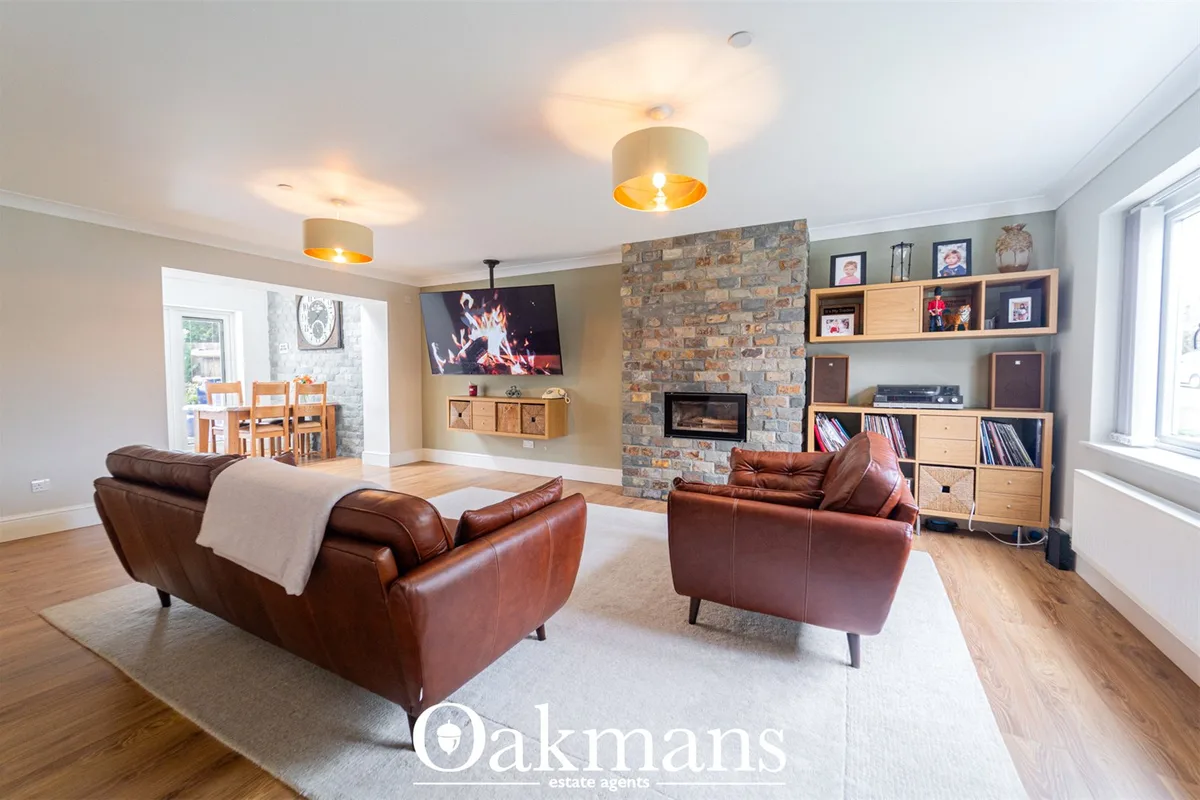 Spacious living room with two brown leather armchairs, exposed brick fireplace, wooden shelving, TV, and wooden flooring