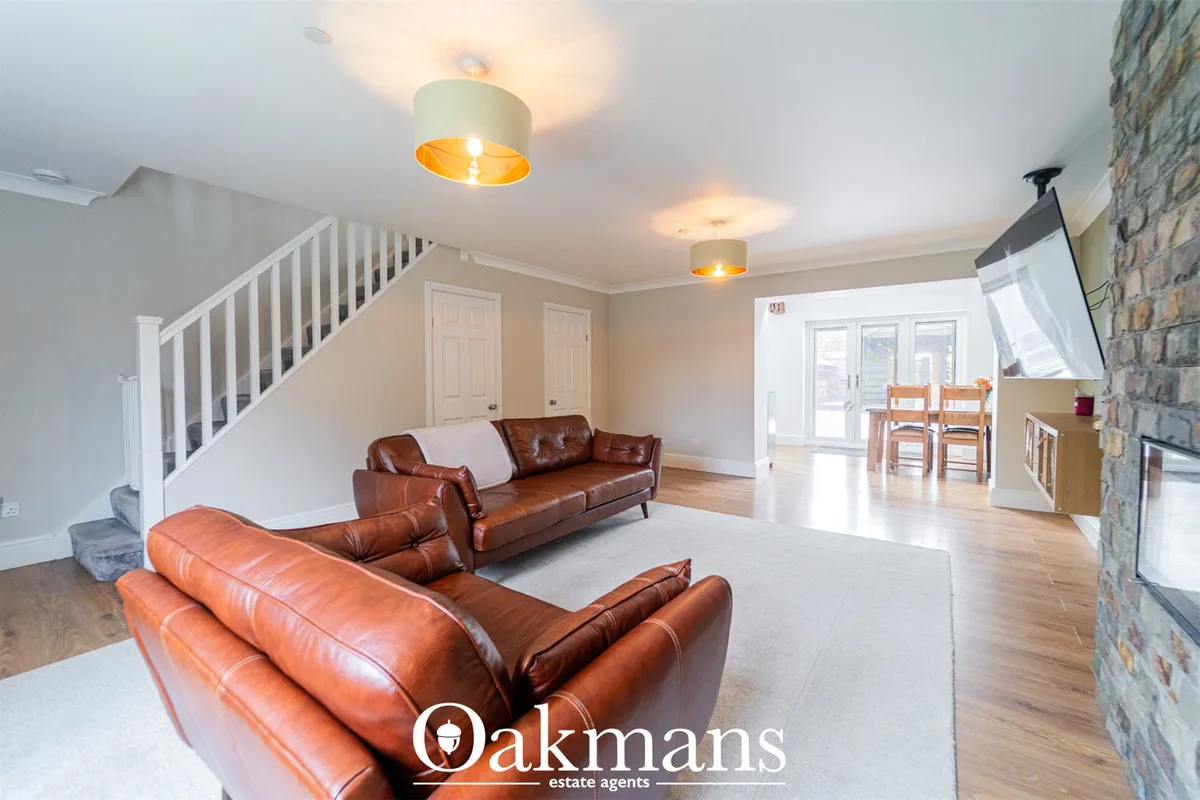 Open-plan living room with two tan leather sofas, wooden flooring, cream ceiling with pendant lights, staircase, and sto