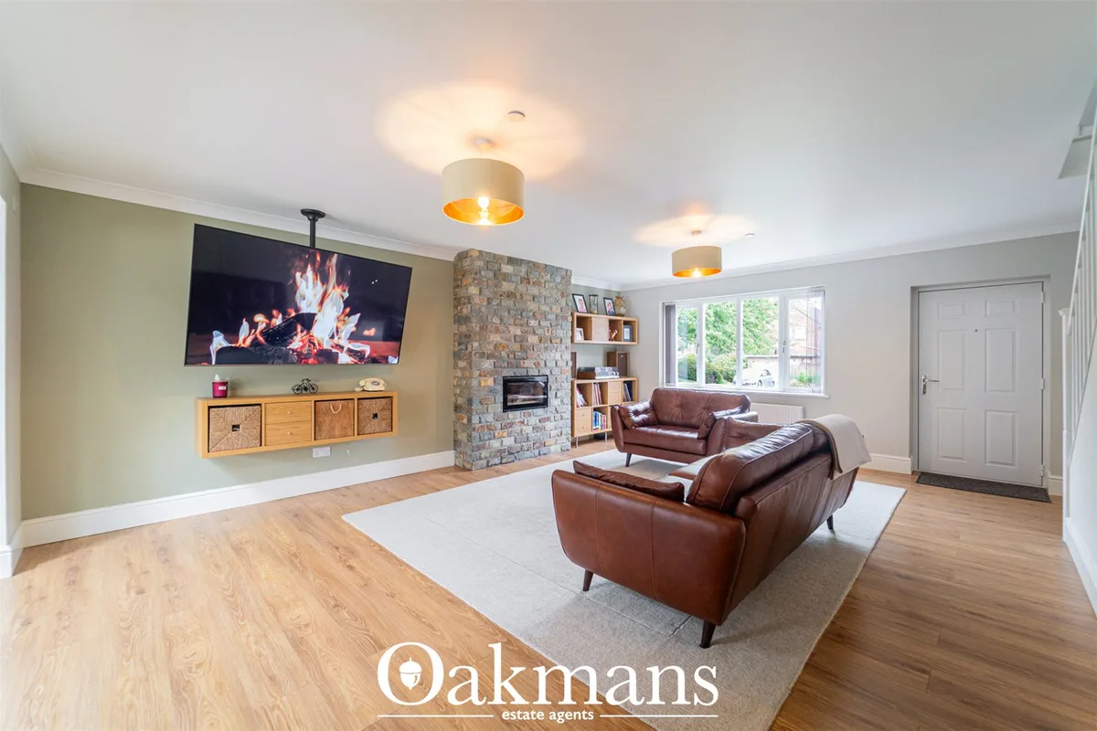 Spacious living room with brown leather furniture, stone fireplace, wall-mounted TV, wooden media unit, and large window