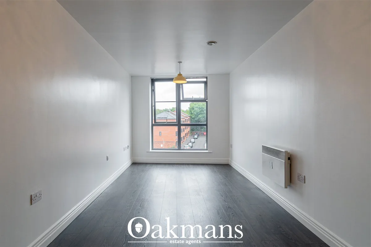Bright empty hallway with dark wood flooring, white walls, pendant light, radiator, window overlooking urban street