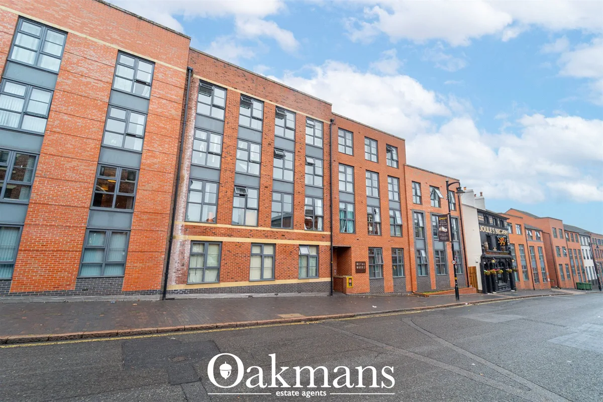 Red brick converted warehouse building with multi-pane windows, gray stone banding, and street frontage under blue sky w