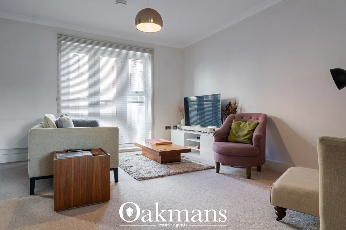 Bright living room with cream and burgundy upholstered seating, wooden coffee table, wall-mounted TV, patio doors with b