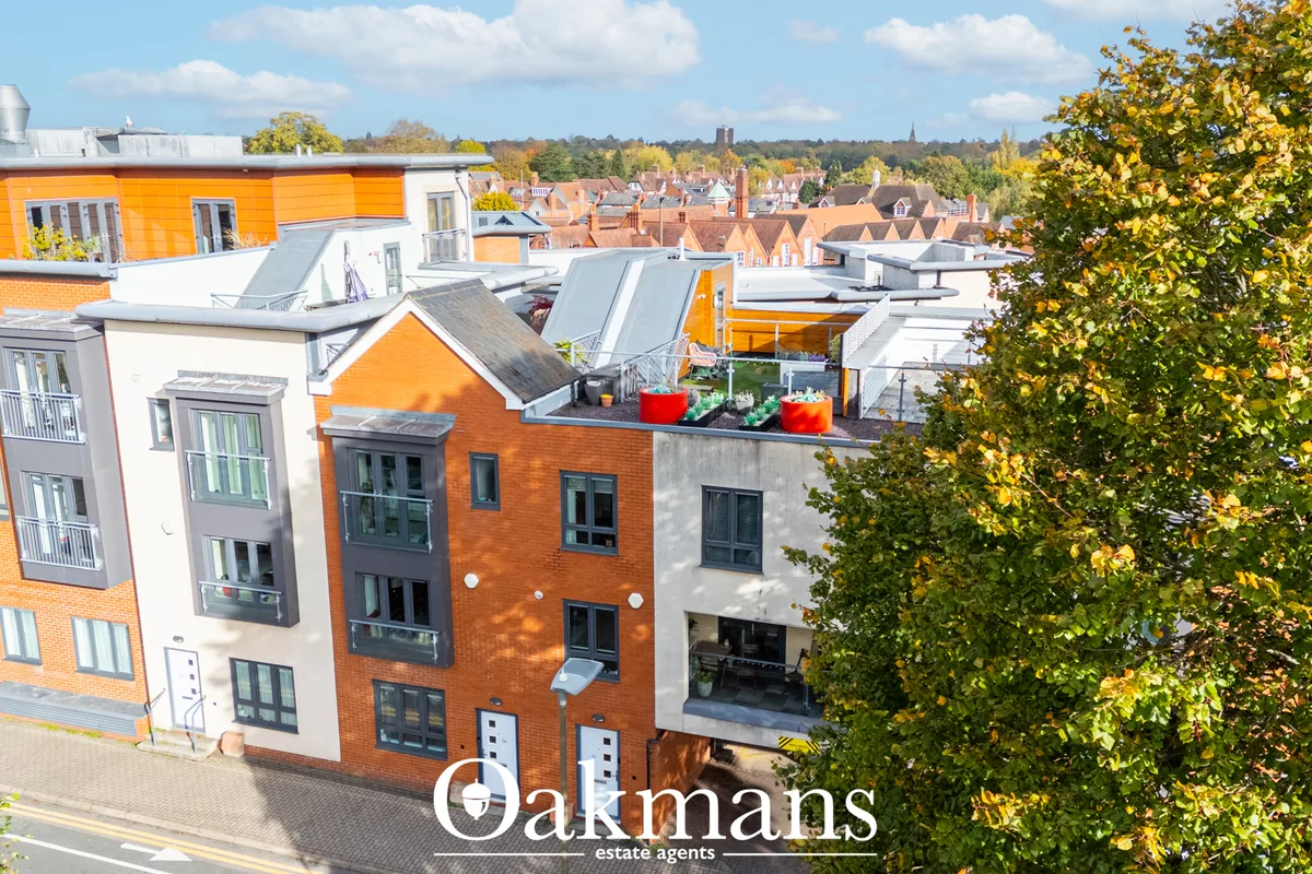Aerial view of modern residential apartment building with orange and white brick facade, rooftop terrace with planters, 