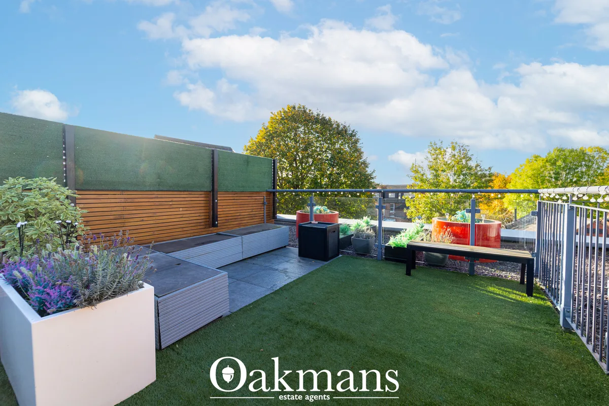 Modern rooftop terrace with decking, artificial lawn, raised planters with purple flowers, seating area, and city skylin