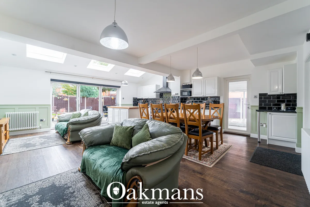 Open-plan living area with green leather sofas, wooden dining table with chairs, black kitchen with skylight, exposed ce