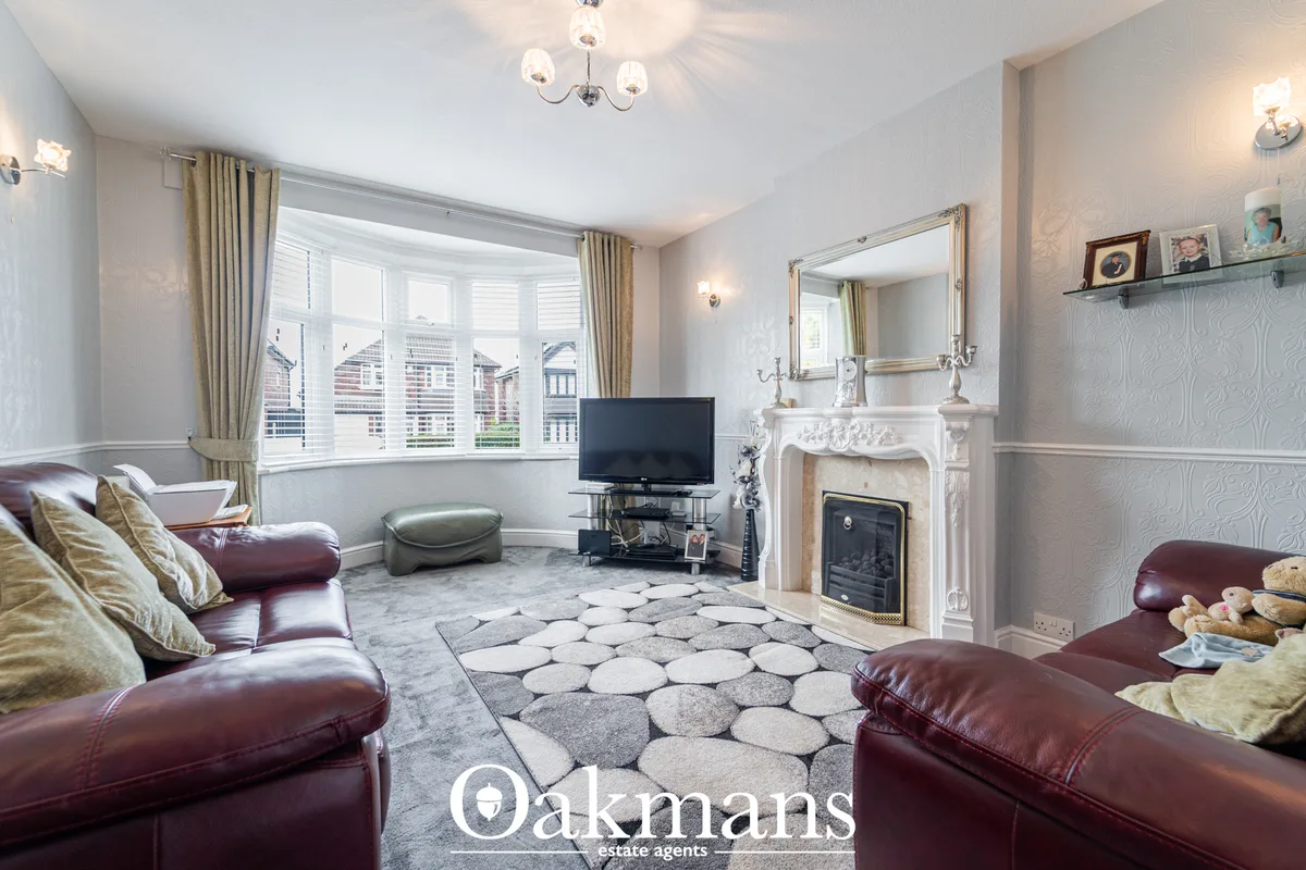 Spacious living room with burgundy leather sofas, decorative fireplace with ornate surround, bay window with gold curtai