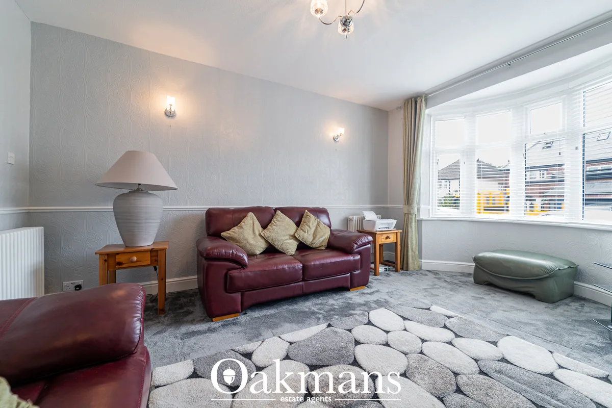 Spacious living room with burgundy leather sofa, beige cushions, grey patterned rug, wooden side tables, ceramic table l