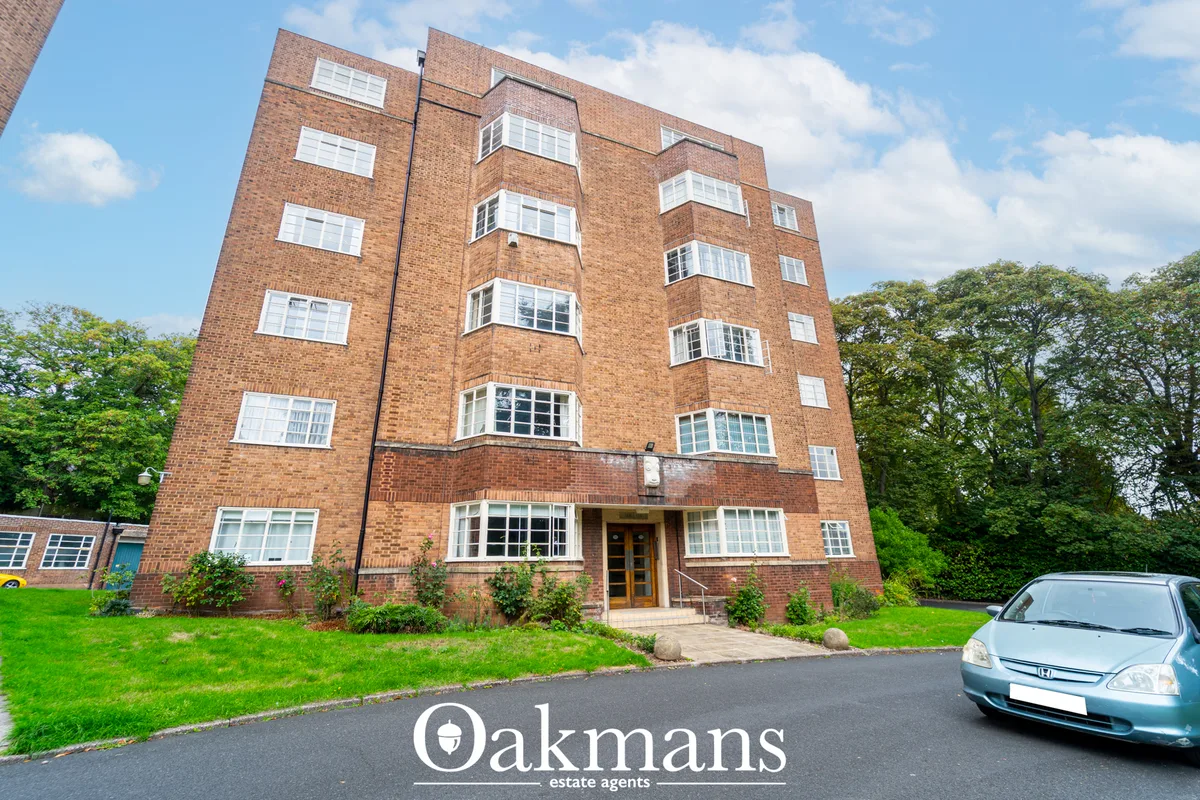 Red-brick apartment building, six storeys, bay windows, manicured lawns, entrance with steps, parked car