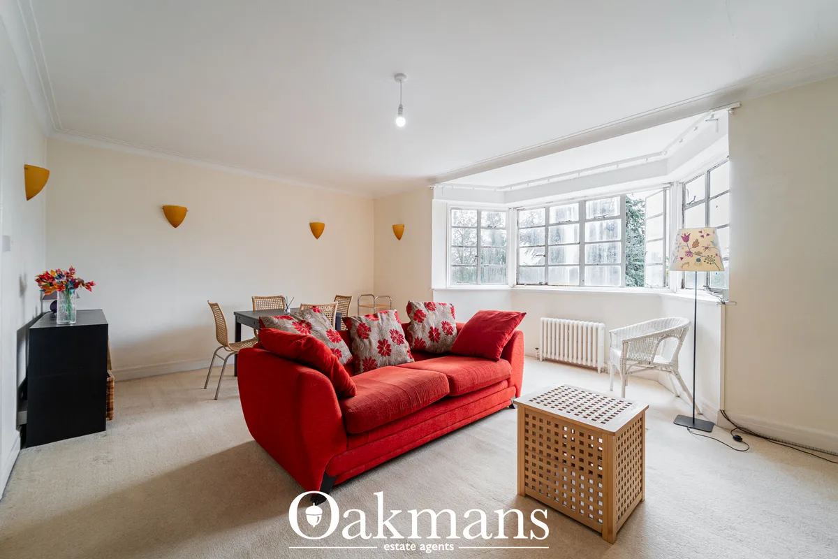 Bright living room with red sofa, patterned cushions, wooden coffee table, large windows overlooking garden, pendant lig