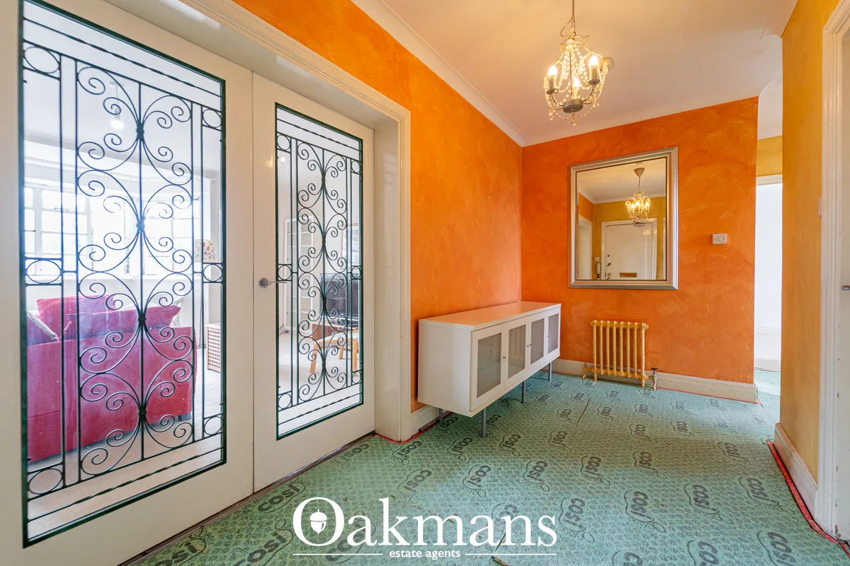 Bright orange hallway with ornate wrought iron doors, white storage unit, mirror, pendant lighting and patterned carpet