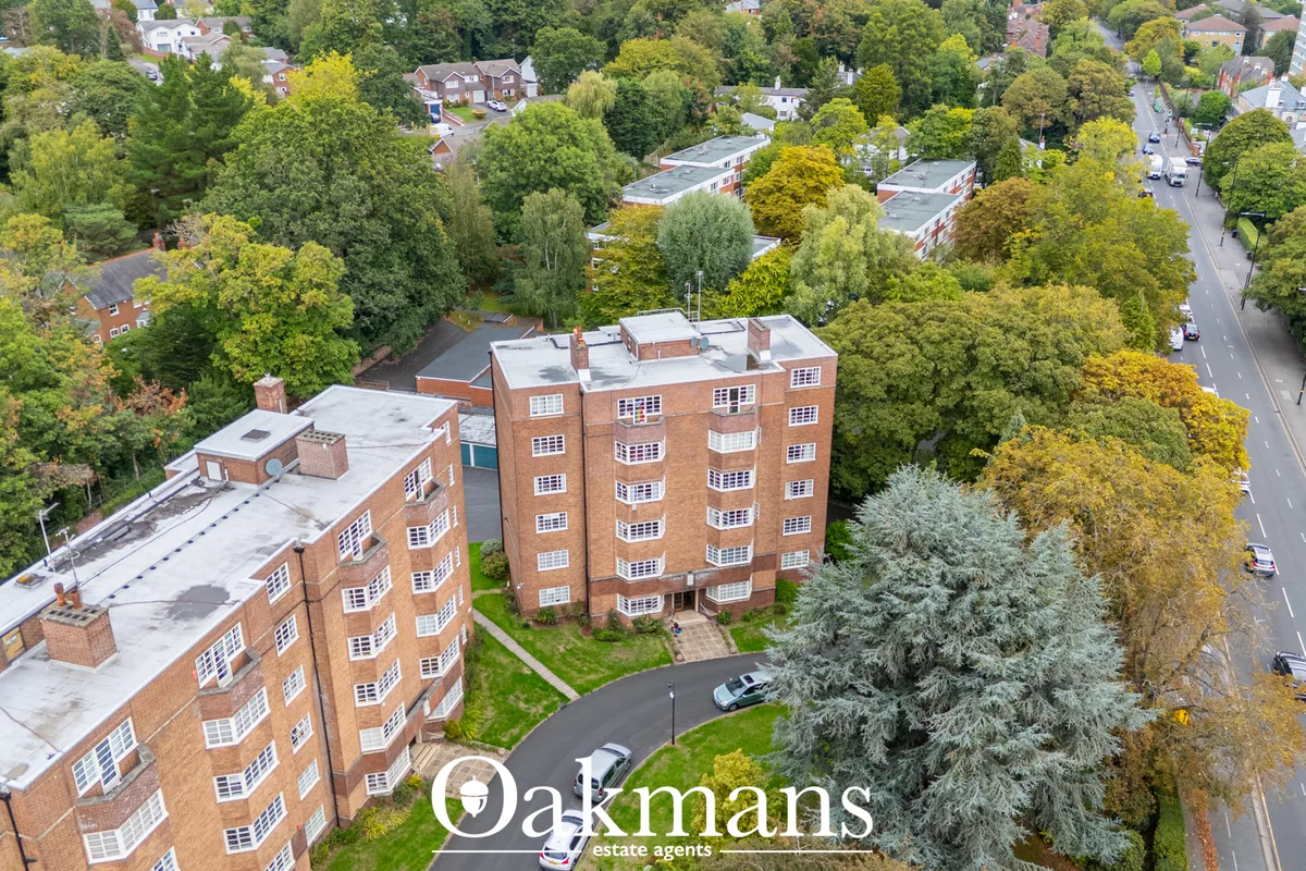 Aerial view of red brick apartment building surrounded by mature trees in suburban residential area
