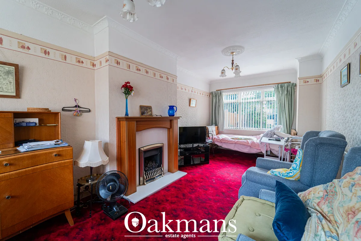 Spacious living room with red carpet, wood fireplace, blue armchairs, vintage furniture, large windows with green curtai