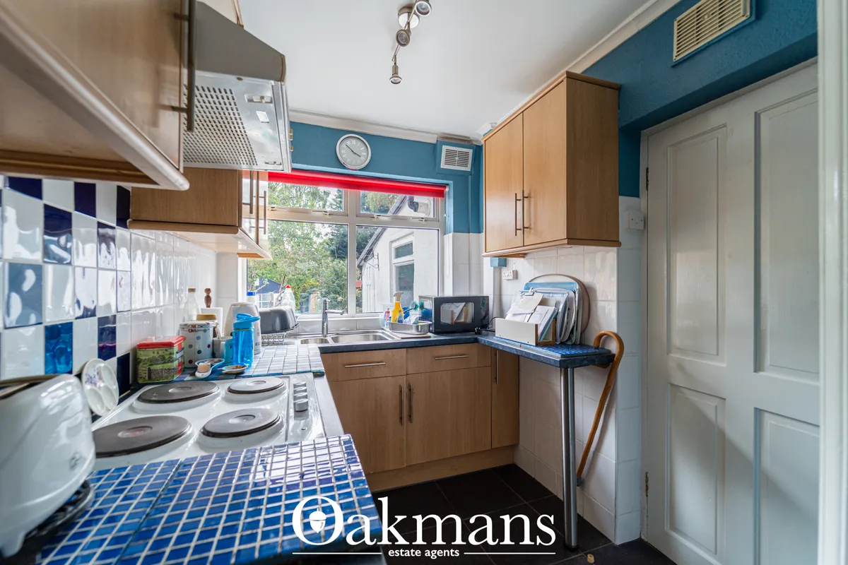 Modern kitchen with oak cabinetry, blue tiled flooring, white tile splashback, electric hob, window overlooking garden a