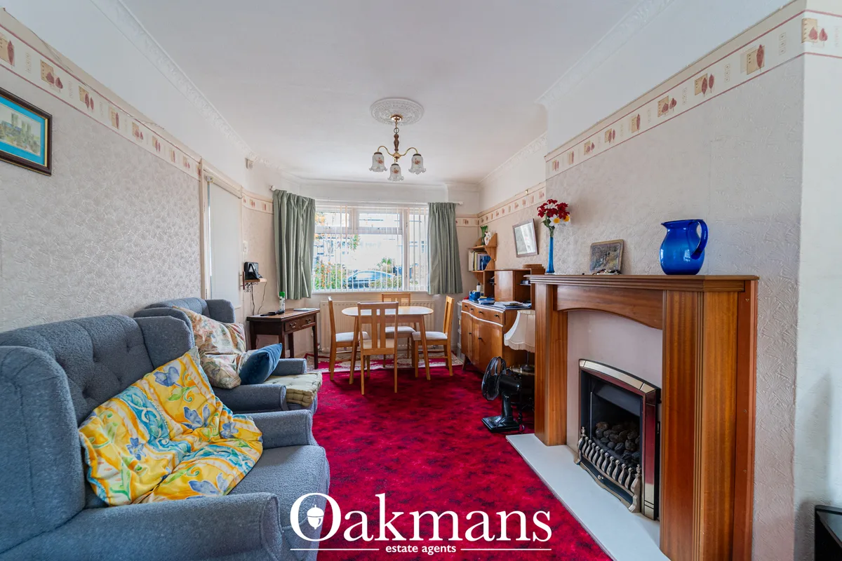 Spacious living room with grey sofa, fireplace, dining table, bay window with green curtains and red carpet