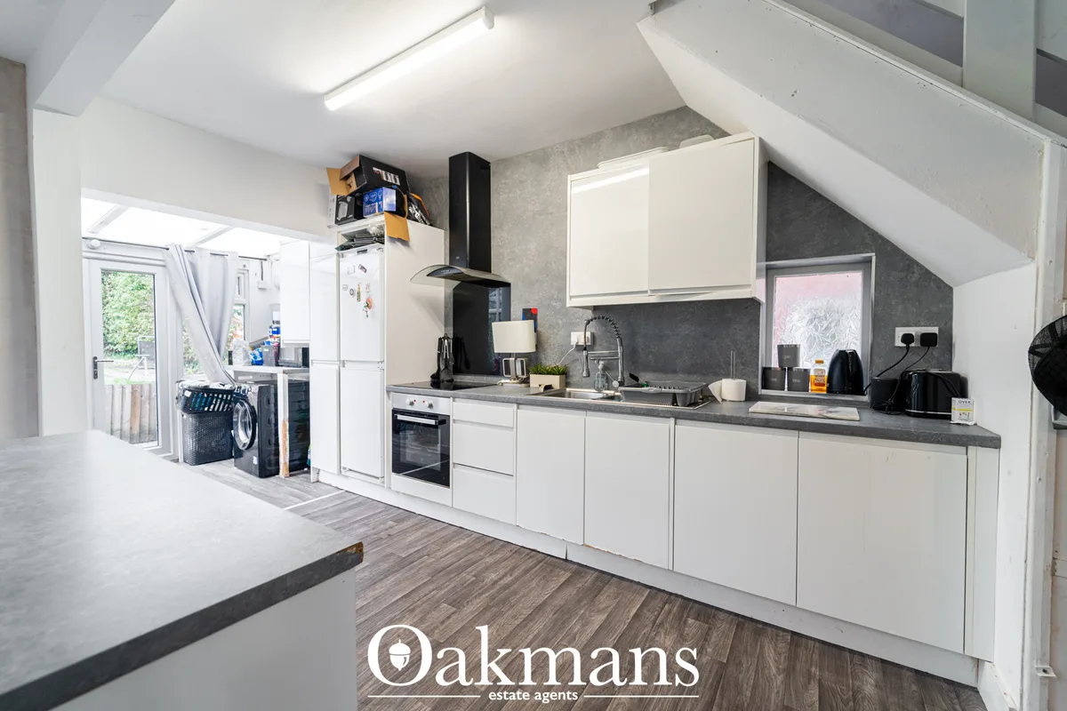 Modern fitted kitchen with white cabinetry, dark grey worktops, black extractor hood, integrated appliances and grey til