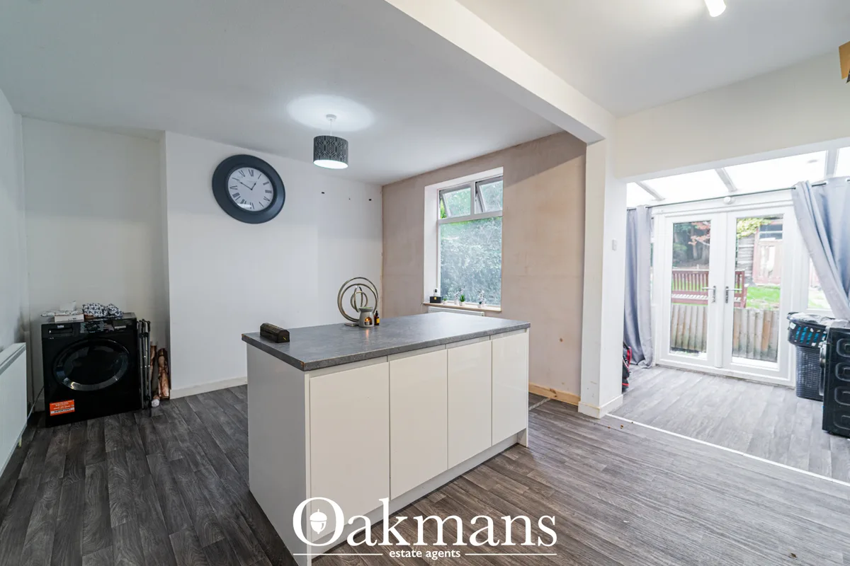 Modern kitchen with cream fitted units, grey worktops, island breakfast bar, pendant lighting, and French doors to garde