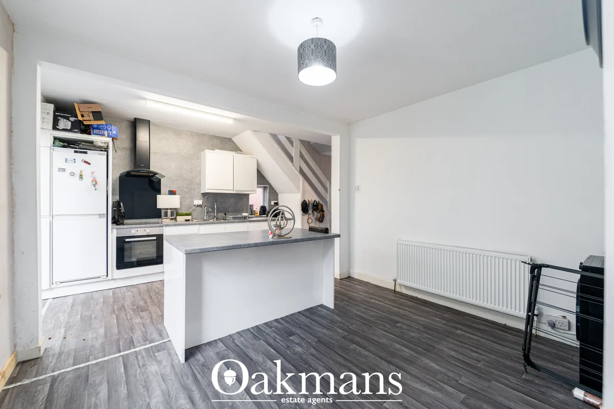 Modern open-plan kitchen with white fitted units, dark worktops, breakfast bar, built-in oven, and adjacent dining area 