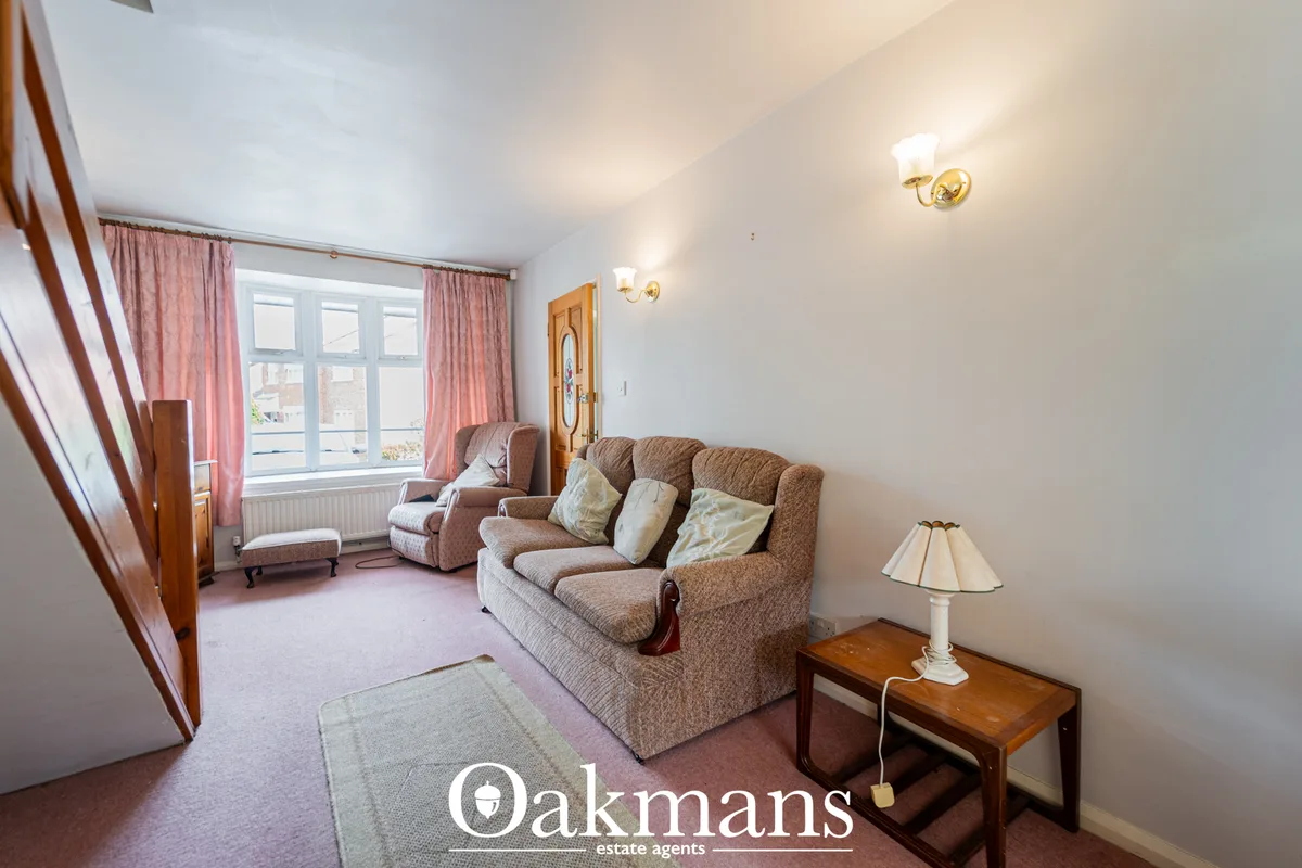 Spacious living room with brown upholstered sofa, matching armchair, wooden side table with lamp, pink curtains, large w
