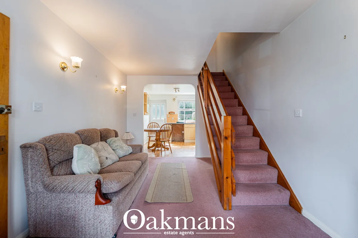 Bright hallway with staircase featuring wooden bannister and burgundy carpet, grey upholstered sofa with cushions, wall 