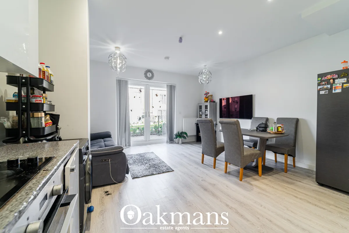 Open-plan living and dining space with grey upholstered chairs, wooden dining table, TV, grey armchair, and full-length 