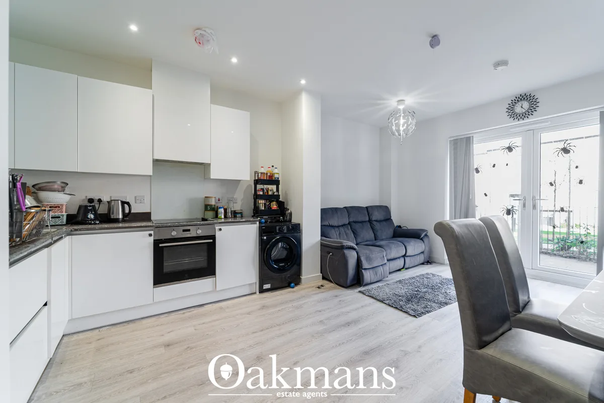 Open-plan living and kitchen space with white fitted units, navy three-seat sofa, grey chair, wooden flooring, and glaze