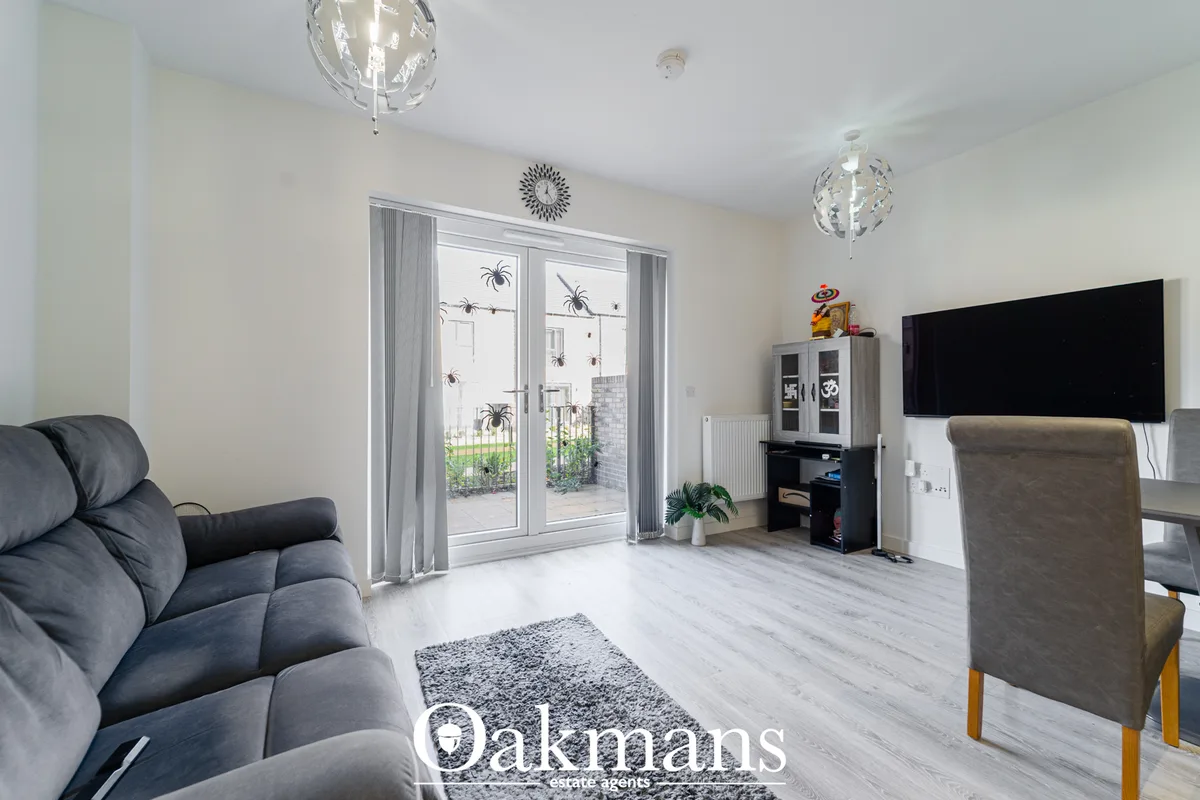 Modern living room with grey upholstered sofa, wall-mounted TV, glass doors to garden, pendant lighting, and light wood 