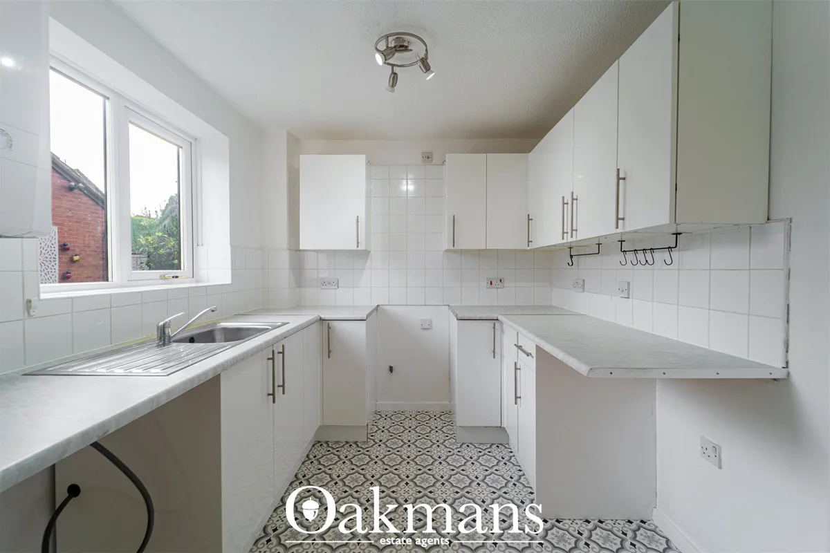 White galley kitchen with fitted units, stainless steel sink, patterned floor tiles and window overlooking garden
