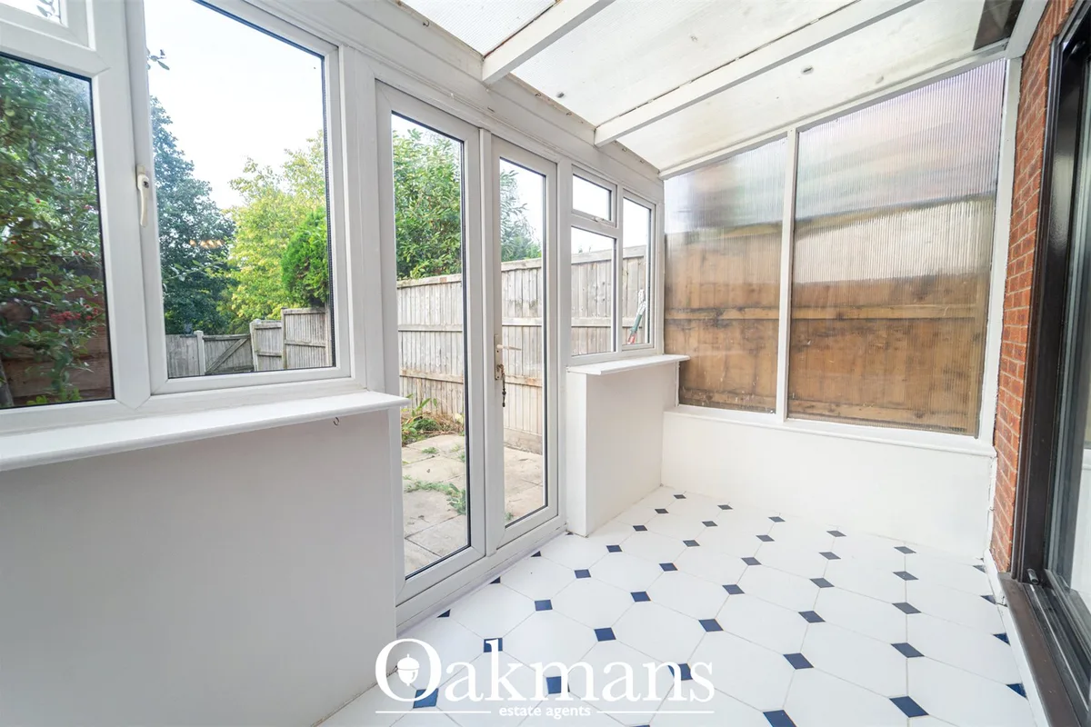 Bright conservatory with white uPVC frame, glazed roof panels, diamond-pattern tiled floor, and views to garden