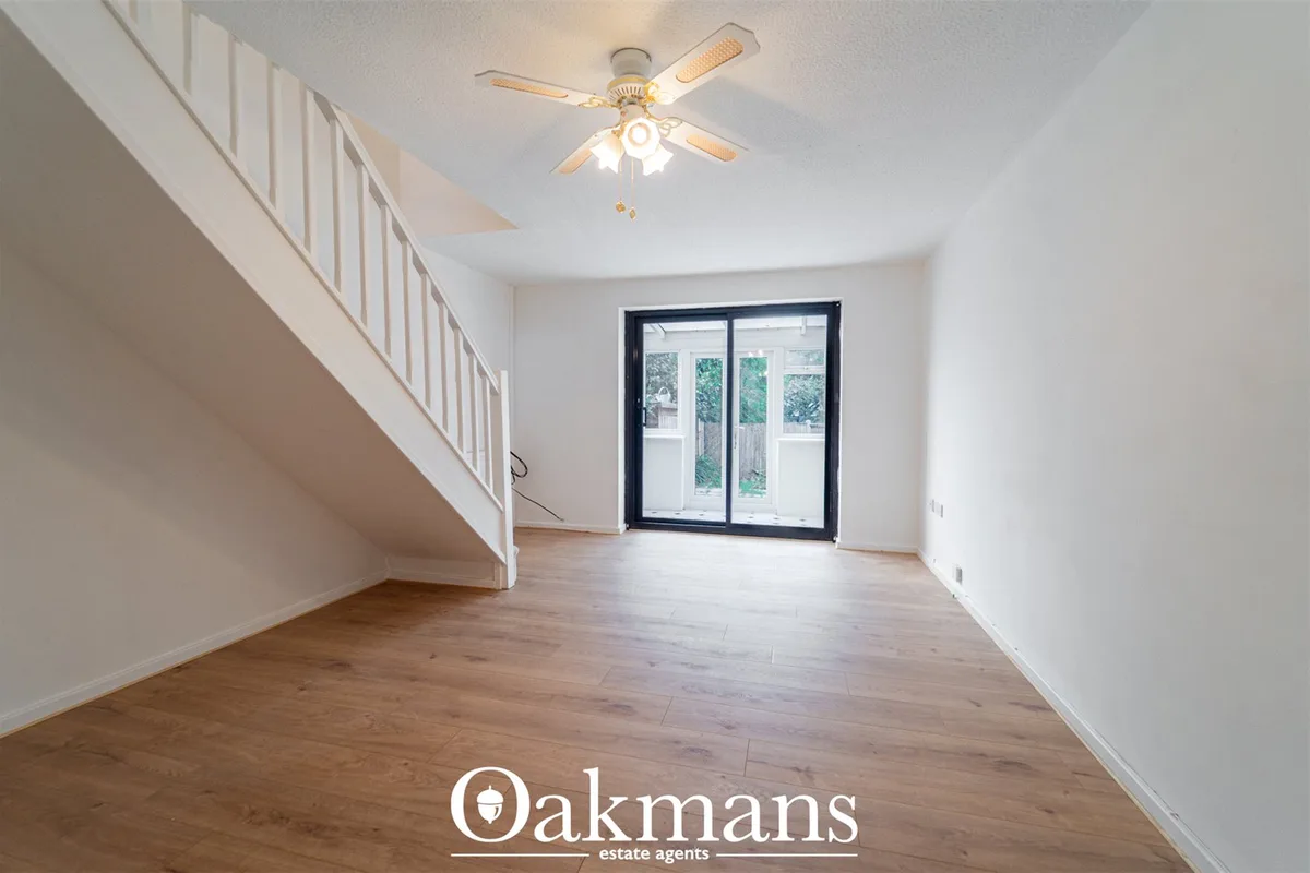Bright open-plan living room with wooden flooring, white walls, ceiling fan with lights, staircase to left, and black-fr