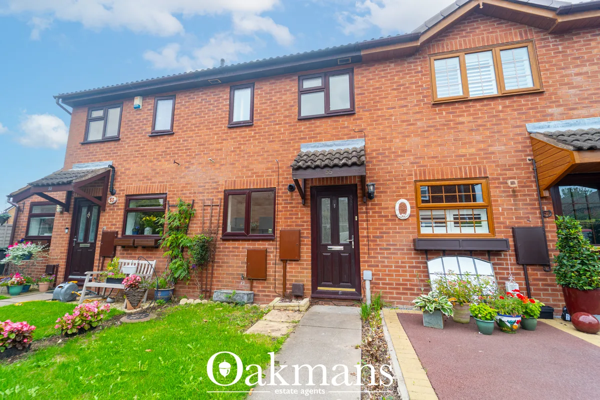 Red brick terraced house with multiple windows, brown doors, manicured front garden with flowering plants and patio