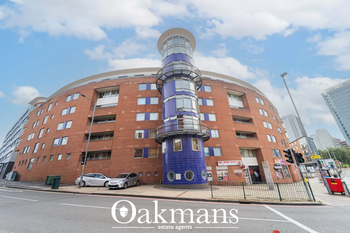 Red brick apartment building with distinctive blue cylindrical tower feature, rounded corners, multiple windows and stre
