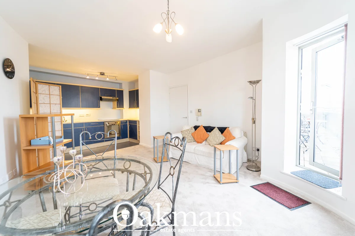 Open-plan living and kitchen area with white sofa, orange cushions, glass dining table with metal chairs, blue kitchen u
