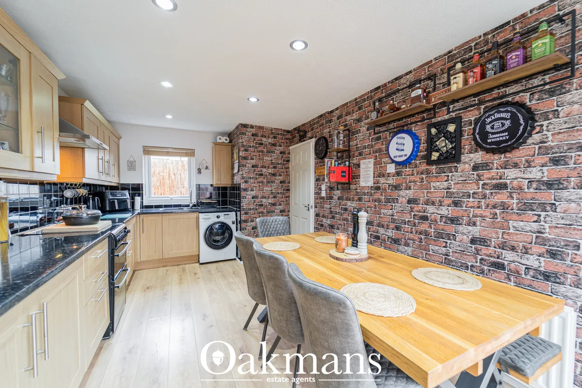 Modern kitchen with light wood cabinets, black worktops, dining table, exposed brick wall with decorative plates and she
