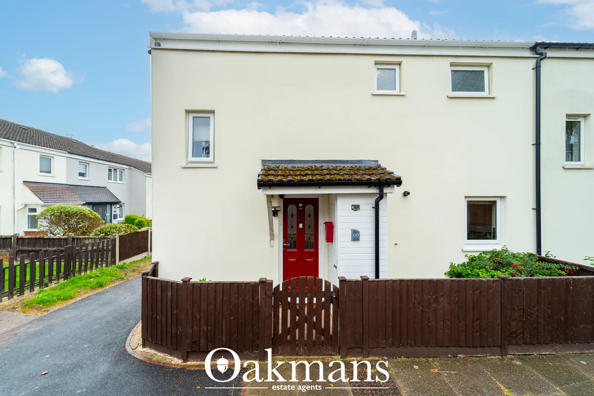 Cream-rendered terraced house with red entrance door, white garage door, moss-covered tiled canopy, brown fence and land