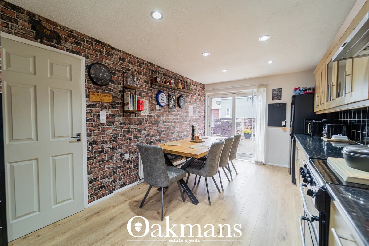 Modern kitchen with exposed brick wall, wooden dining table, grey upholstered chairs, cream cabinetry, black countertops