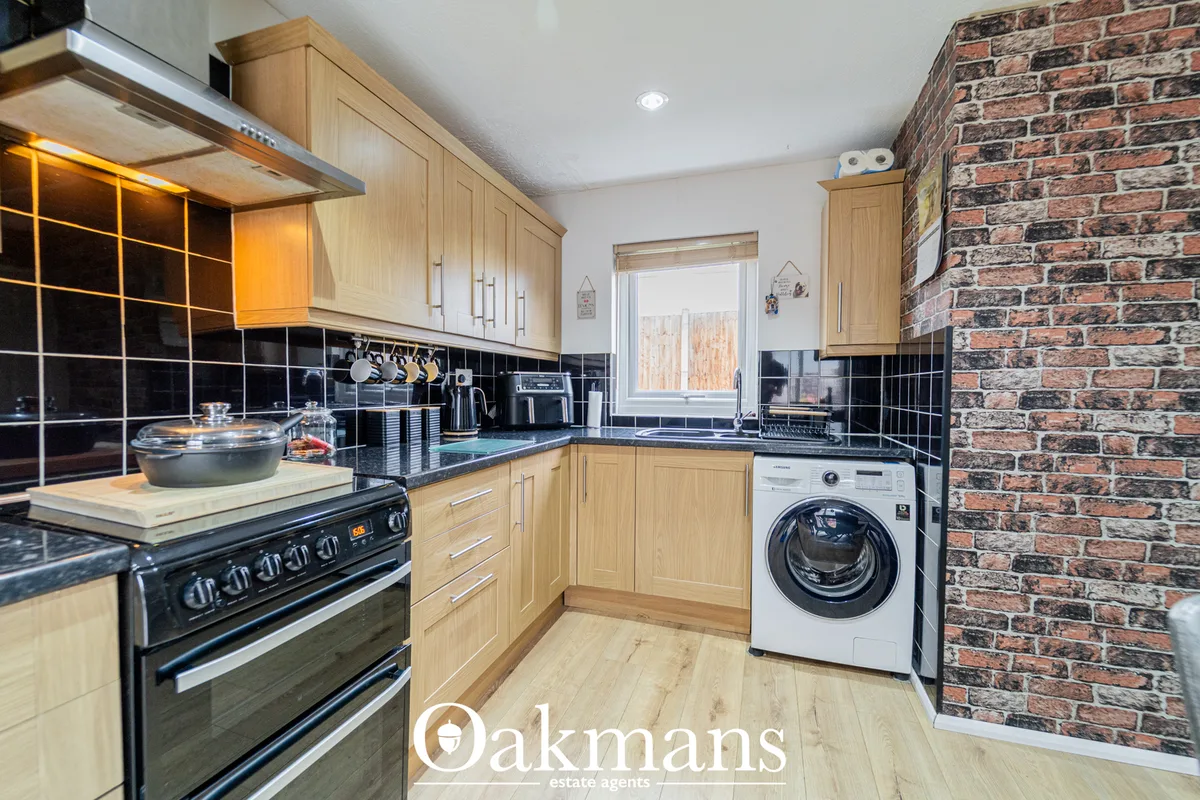 Modern fitted kitchen with oak cabinetry, black tile splashback, granite worktops, integrated appliances and exposed bri