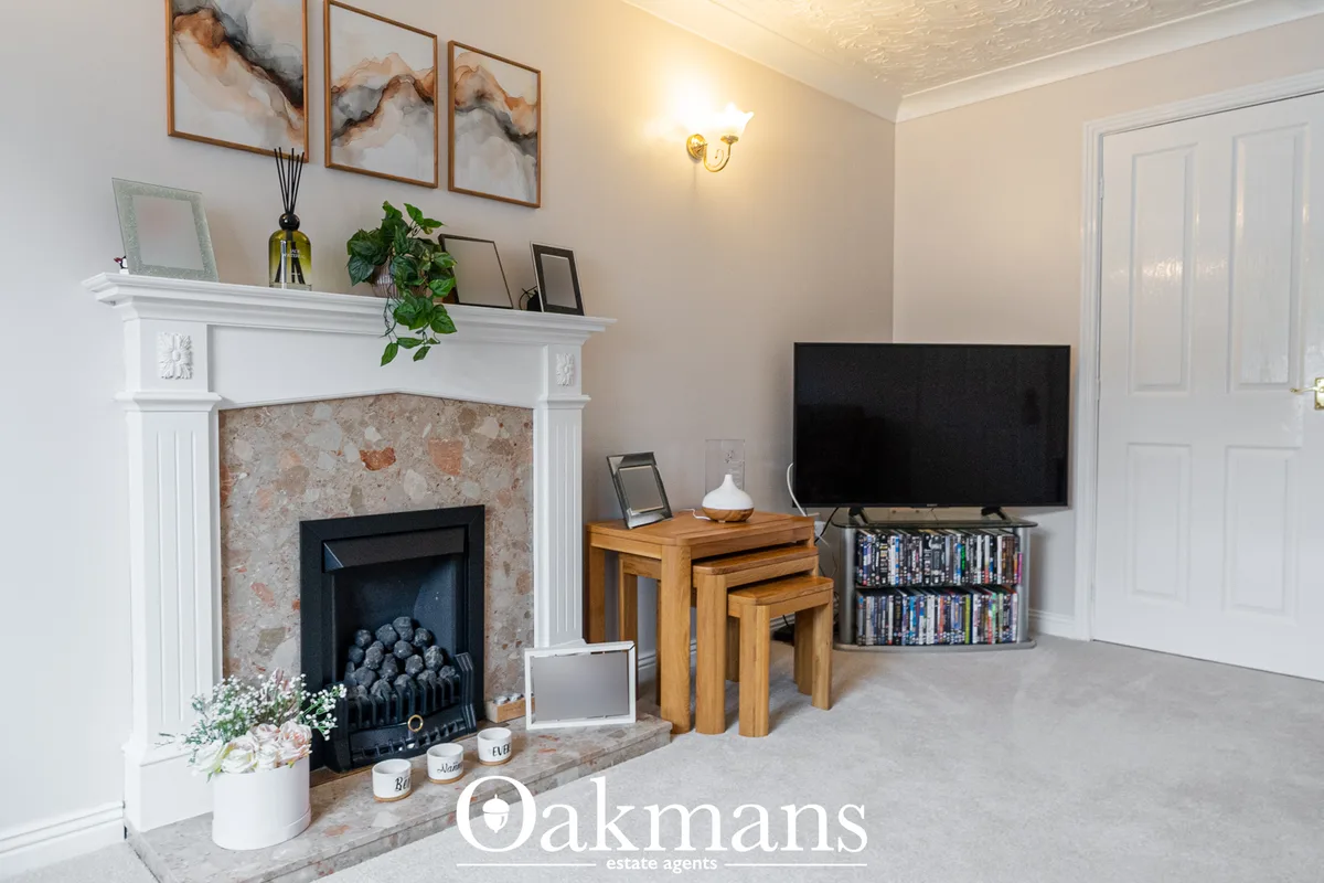 Modern living room with fireplace, TV on wall, wooden nesting tables, bookshelf, and elegant décor