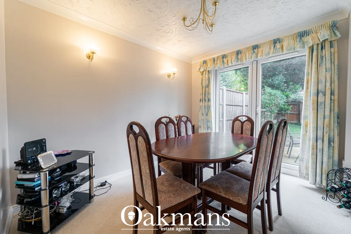 Formal dining room with dark wood table, six upholstered chairs, patio doors to garden, patterned curtains and period ce