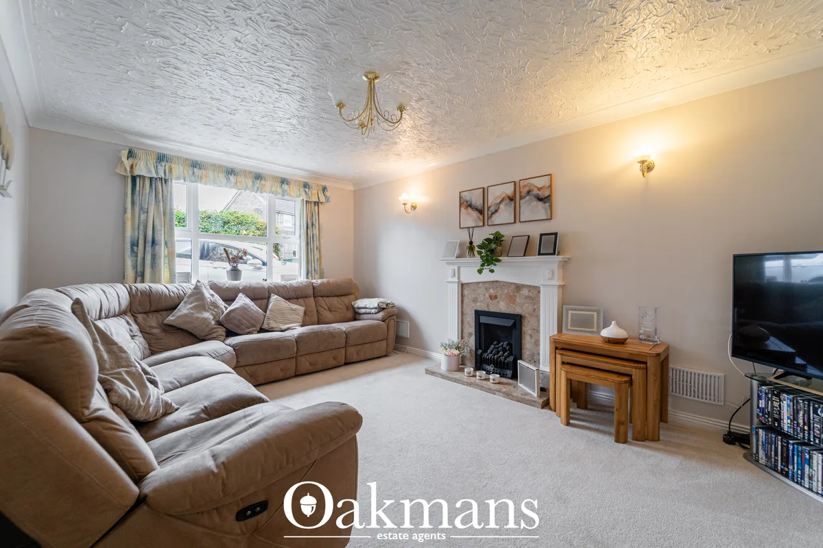 Spacious living room with beige leather reclining sofa, fireplace with white mantel, flat-screen TV, wooden side tables,