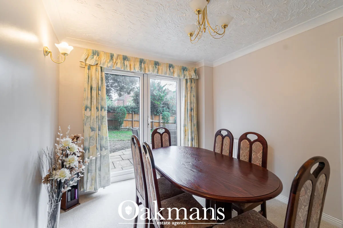 Elegant dining room with oval dark wood table, upholstered chairs, patio doors opening to garden, patterned curtains and
