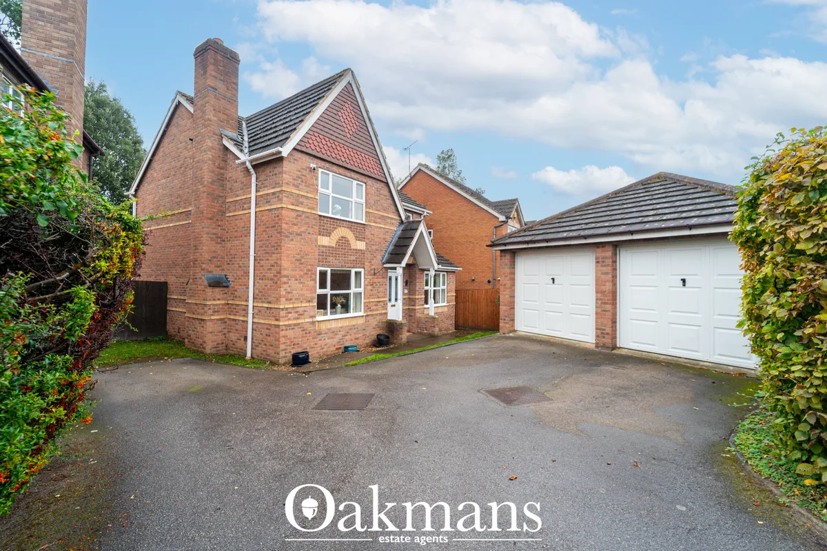 Front elevation of red brick detached house with pitched roof, white windows, double garage, driveway and hedged boundar